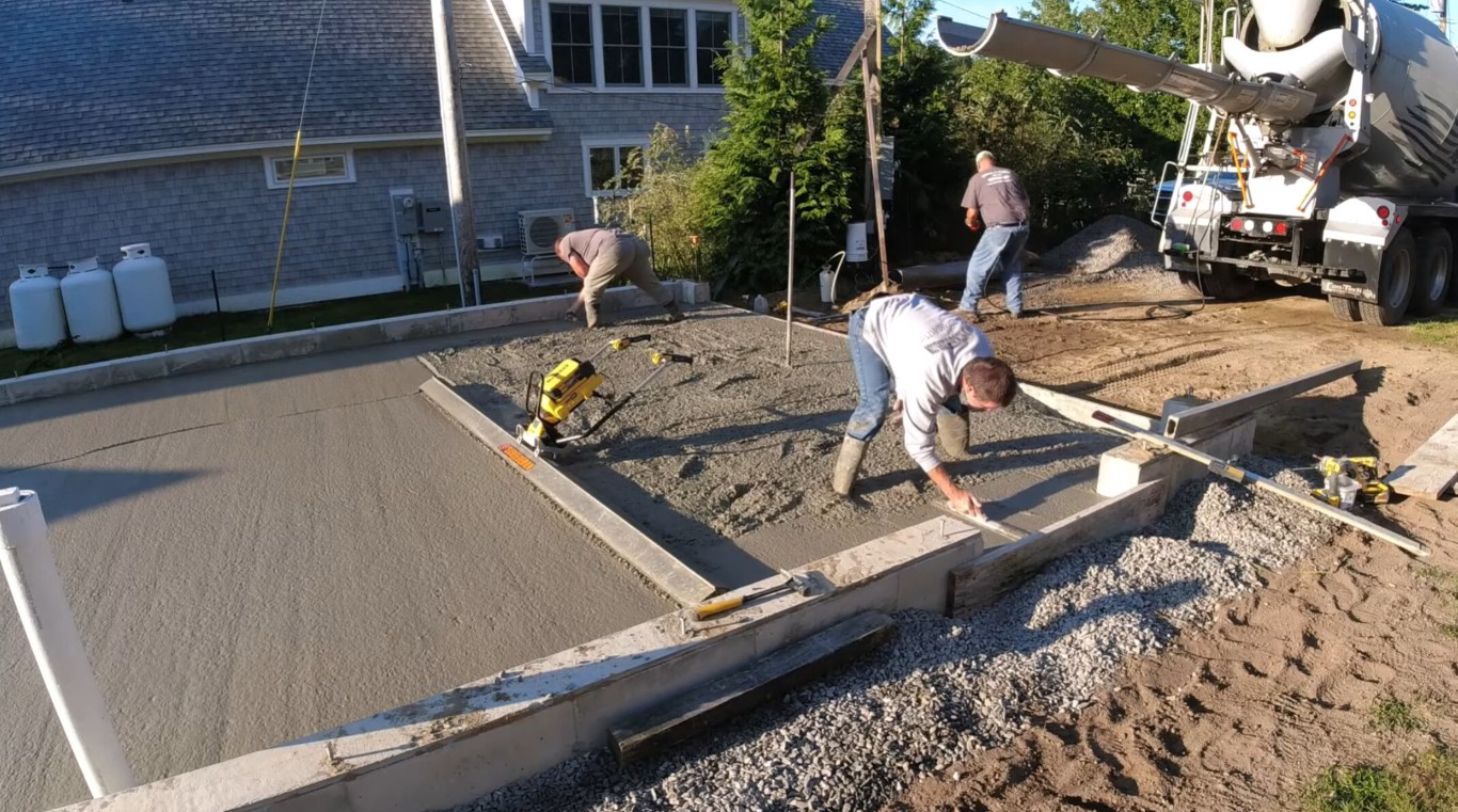Crew screeding a freshly poured concrete driveway with a mixer truck on site